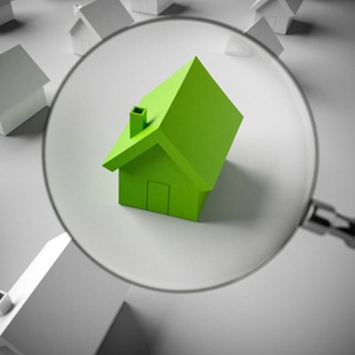 Ökologische Kennwerte Hochbau Ein grünes Hausmodell, welches durch eine Lupe vergrößert ist