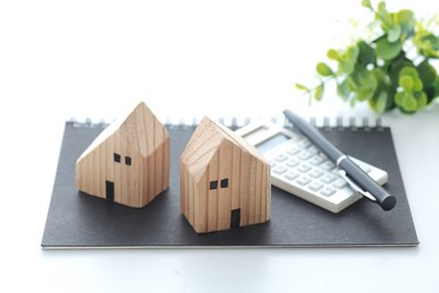 Hochbau Zwei Modell-Holzhäuser stehen auf einer Mappe, auf der auch ein Taschenrechner und ein Stift liegen