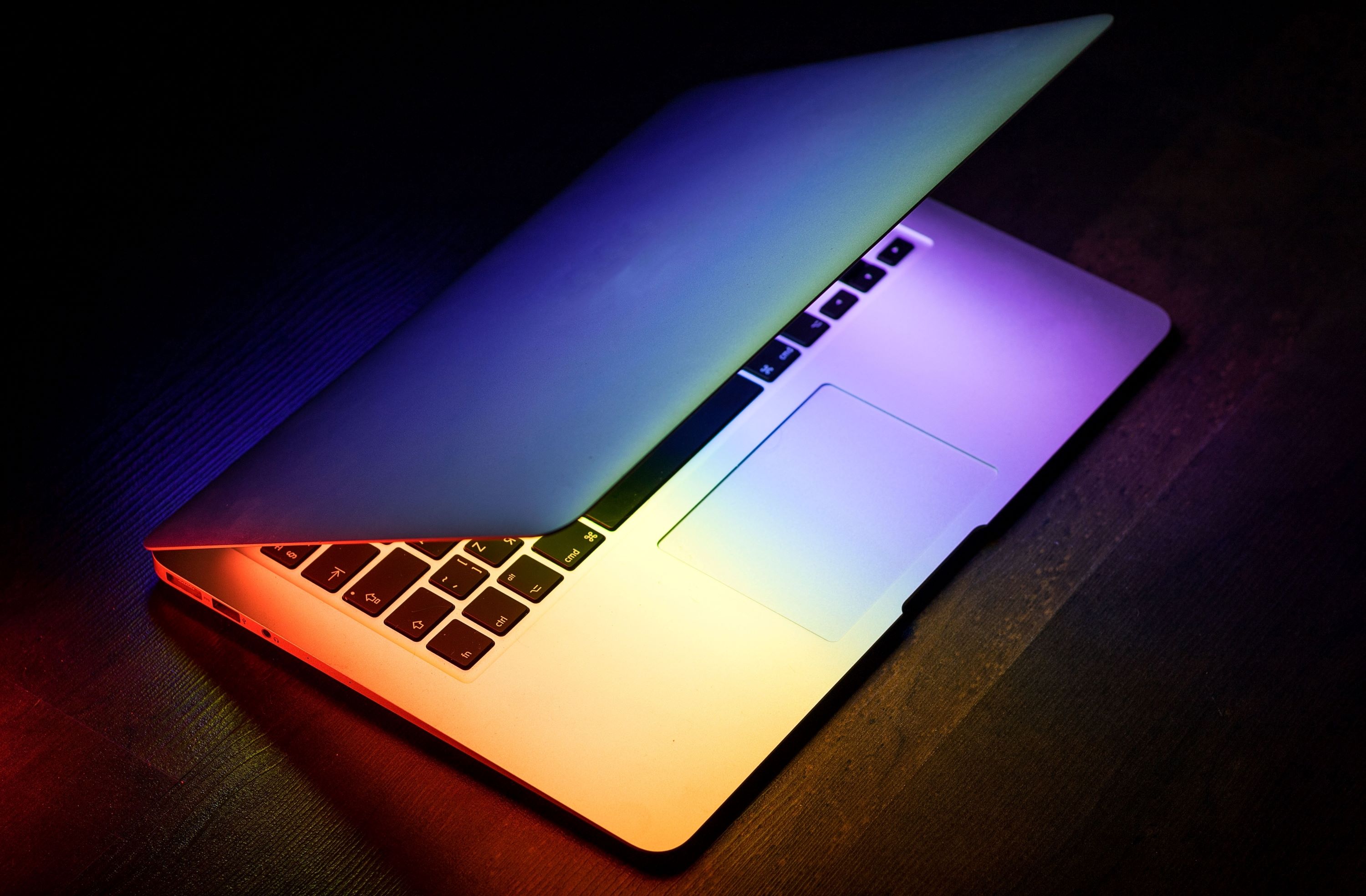 Jahresrelease Halb geöffneter Laptop auf dunklem Tisch mit farbiger Lichtreflexion auf der Tastatur